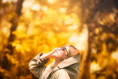 Mutlu kadın yaprak atıyor. Sonbahar parkında yaprakları ile eğlenen sezon ve güzel mutlu genç kadın
