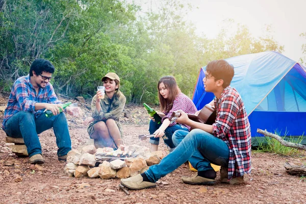 Happy friends camping party playing music and enjoying bonfire in nature and lake, Partying in camping, Asian Young people celebrating during summer vacation, summertime and travel activity concepts