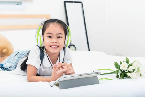 亚洲小女孩在家里的床上用绿色耳机听平板电脑的音乐 通过倾听儿童和增强儿童想象力进行教育 — 图库照片