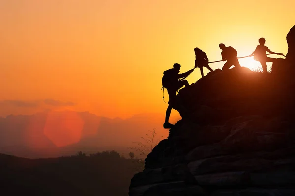 夕日の中で登っている間 登山チームのシルエットが助け合っています 援助の概念 — ストック写真