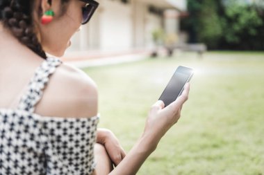 Asyalı kız oturuyor ve bahçede cep telefonu kullanıyor. Sosyal ağ hizmeti kavramı.