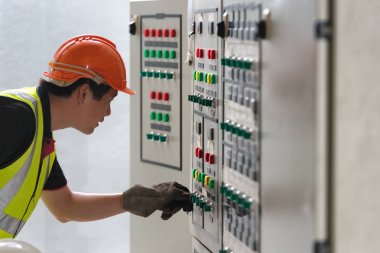 Santralin kontrol odasında Ana Dağıtım Kurulu paneline bakan elektrikçi gençler.
