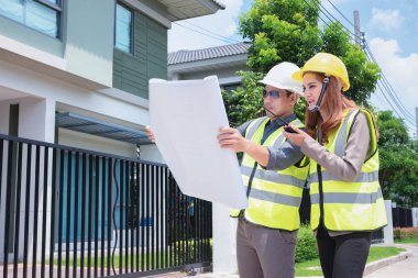 Asyalı mühendisler müşterilerine teslim için hazırlamak için ev müfettişleri ile planı tartışırken ellerinde plan tutan.