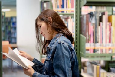 Uluslararası Kolej/Üniversite Kütüphanesi'ndeki kitaplıktan Asyalı kız öğrenci açık ve öğrenme ders kitabı.
