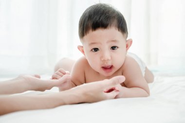 Asya gülümseyen erkek bebek oyun ve oturma odasında annesine sürünerek, Anne birlikte bebek emin hissetmesine yardımcı olmak için el uzatmak. Bebek becerileri kavramı geliştirmek.