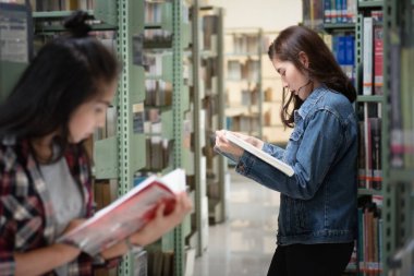 Uluslararası Kolej/Üniversite Kütüphanesi'ndeki kitaplıktan Asyalı kız öğrenci açık ve öğrenme ders kitabı.