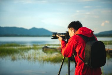 Seyahat fotoğrafçısı sehpa üzerinde kamera ile gün batımında göl doğa ile bir fotoğraf çekmek, dikkat doğa dağ manzarası ve göl odaklama, Doğal fotoğrafçılık rahatlatıcı kavramı.