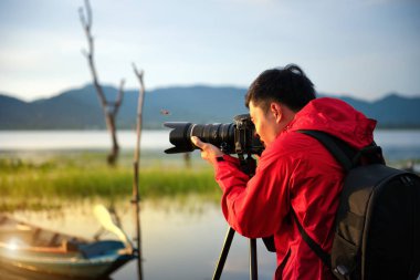 Seyahat fotoğrafçısı sehpa üzerinde kamera ile gün batımında göl doğa ile bir fotoğraf çekmek, dikkat doğa dağ manzarası ve göl odaklama, Doğal fotoğrafçılık rahatlatıcı kavramı.