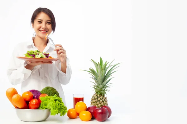 亚洲年轻女子拿着沙拉蔬菜与新鲜水果和健康的饮食在桌子上 — 图库照片