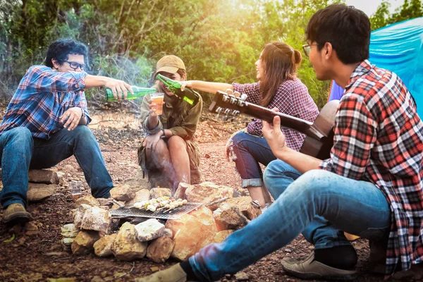 Happy friends camping party playing music and enjoying bonfire in nature and lake, Partying in camping, Asian Young people celebrating during summer vacation, summertime and travel activity concepts