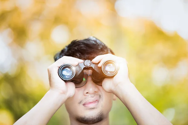 Asian young looking through his binoculars and blinking with sunlight. Eyes Damage. Short term eye problems. Selection focus holding binoculars.