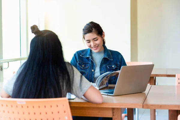 亚洲女学生打开阅读杂志和微笑放松与笔记本电脑在木桌上在学院 大学图书馆 — 图库照片