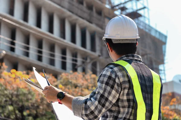 Engineering Consulting People on construction site holding blueprint in his hand. Building inspector. Construction site check drawing and business workflow of new highrise building.