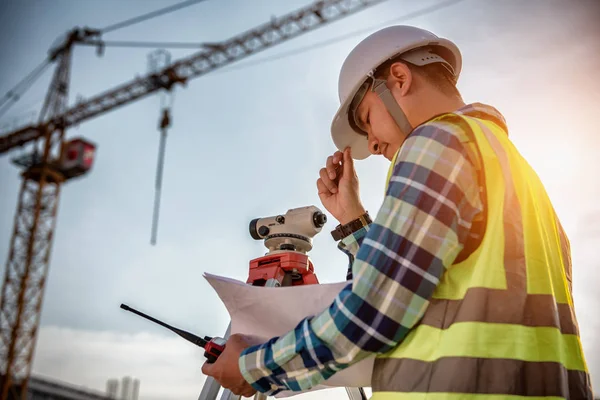 Civil Engineering, Surveyor people making on construction site and holding blueprint in his hand for checking with surveying telescope instrument
