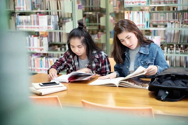 两名亚洲女学生打开在图书馆的房间里读课本 在国际学院 大学学习和友谊的生活 — 图库照片