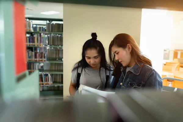 亚洲学生在国际学院 大学图书馆的书架上寻找课本 为大学考试的问题找到正确答案 — 图库照片