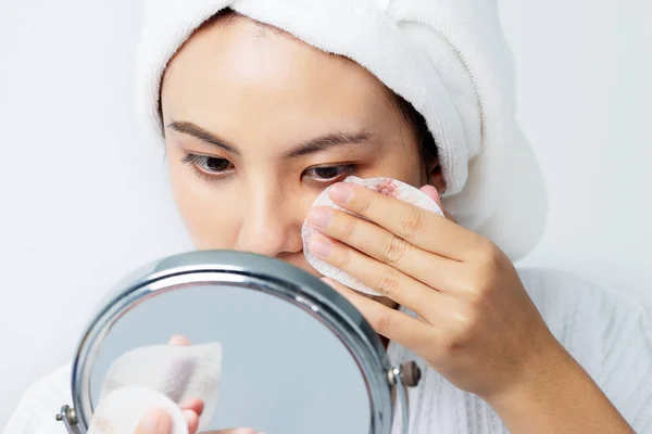 Beautiful skin care concept. Asian beautiful young woman focusing cleaning her face skin with Cotton Pad and looking the mirror.