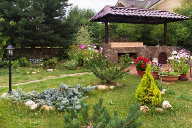 Arka bahçe veranda alan şömine ve mobilya ile. Yeşil parti alanı. Barbekü alanı. Yeşil çim ve çam ağaçları.