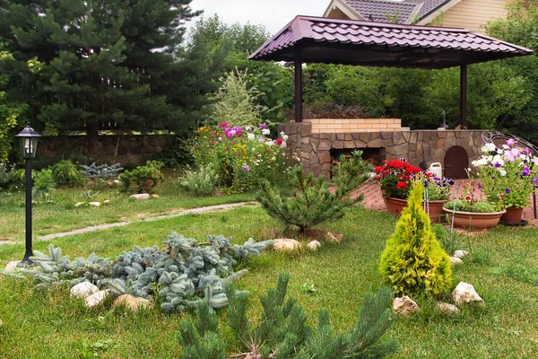 Arka bahçe veranda alan şömine ve mobilya ile. Yeşil parti alanı. Barbekü alanı. Yeşil çim ve çam ağaçları.