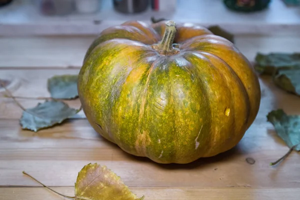 Big yellow-green Pumpkin and fallen leaves on rustic wooden table.Halloween or thanksgiving day