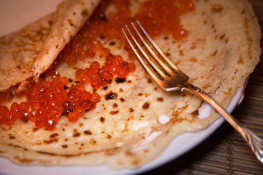 Traditional Russian pancake with red caviar. Fork, wooden table. Maslenitsa. Selective focus.