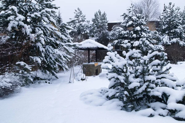 Backyard Patio.Landscape  with barbeque area, snowbanks of white snow, pine trees in country garden. Country life concept.