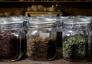 Çay koleksiyonu. Cam kavanozlarda kırmızı, yeşil çay. Ahşap masada kuru çay ile cam kavanozlar.
