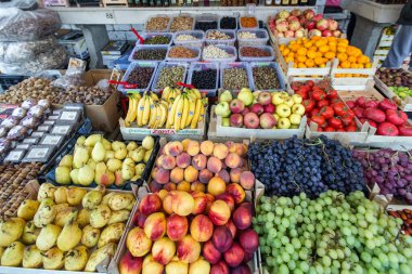 Farklı renklerde taze meyve ve sebzelerle dolu bir market tezgahı. Plastik kutularda taze patates ve sebzeler.