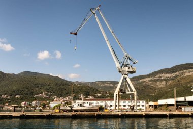 Vinçler Kotor Körfezi 'ndeki kargo terminalinde. Karadağ limanında vinçler ve tekneler var. Dağlar, kasaba, arka plan olarak mavi gökyüzü.
