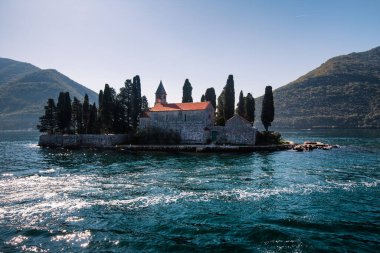 Adriyatik Denizi 'ndeki bir adada Katolik kırmızı çatı ortaçağ manastırı, çan kulesi, duvar ve selvi ağaçları. Karadağ dağları arasında Kotor Körfezi 'nin mavi sularındaki küçük ada. Ada manzarası