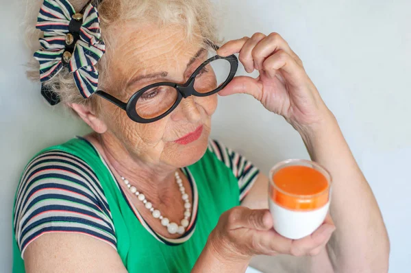 Die reife, runzelige Hipsterfrau mit der lustigen Brille begutachtet ein Glas Gesichtscreme. Hautpflege für Frauen 60-70 Jahre. Frauengesundheit — Stockfoto