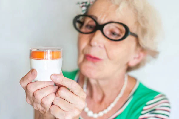 Die reife, runzelige Hipsterfrau mit der lustigen Brille begutachtet ein Glas Gesichtscreme. Hautpflege für Frauen 60-70 Jahre. Frauengesundheit — Stockfoto