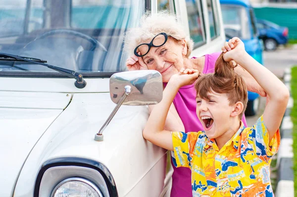 Riendo abuela con su nieto tonteando delante de un espejo de coche. Vacaciones de verano y viajes —  Fotos de Stock