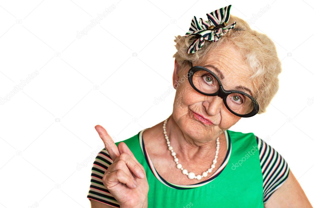 An old wrinkled hipster woman in glasses points her finger to the side with a surprised expression on her face. Isolate. Advertising space. Isolated