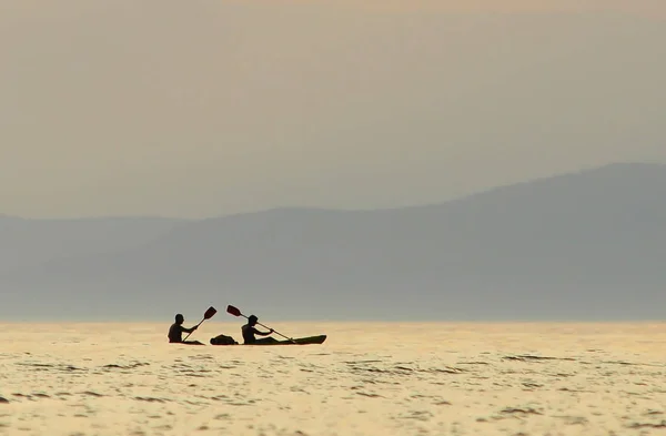 Gün batımında iki kişi deniz kanosinde yüzer.