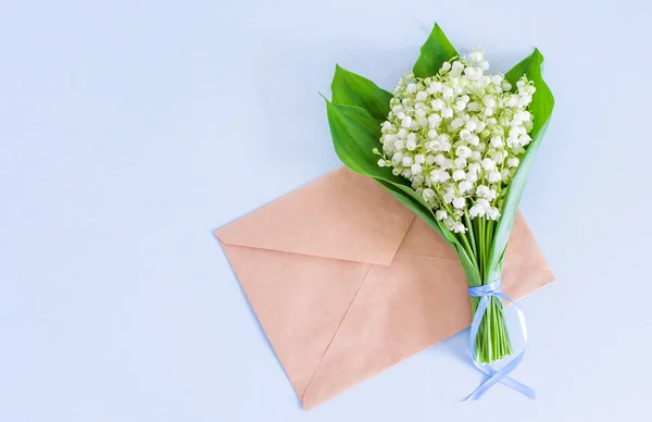 A bouquet of lilies of the valley on a blue background, tied with a ribbon and an envelope from Kraft paper. Top view, empty space for text.