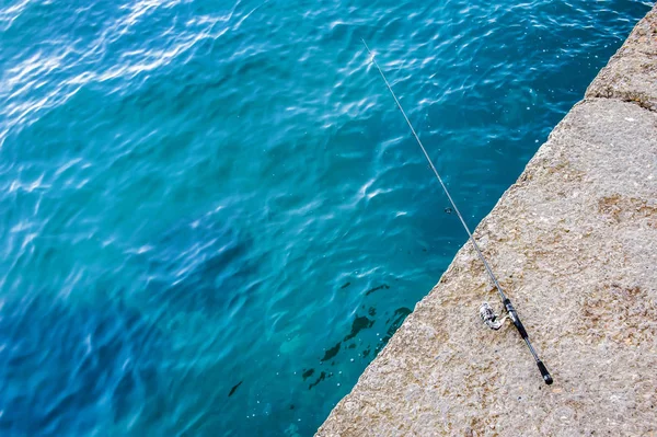 Fishing rod lies on a stone shore against the background of the sea