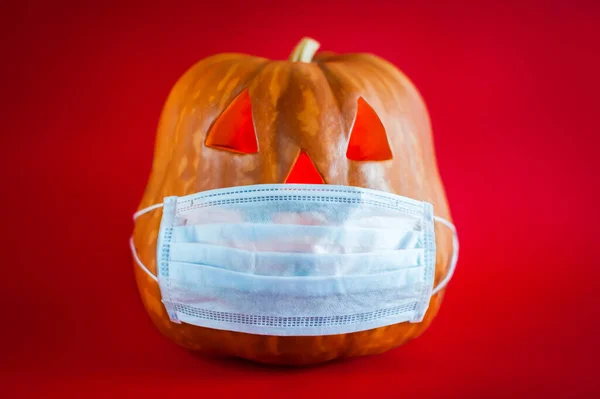 Halloween pumpkin in a protective medical mask on a red background