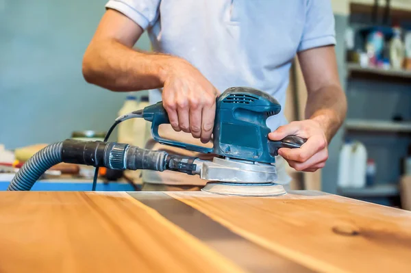 Man works with an electric grinder. Crafts a wooden tabletop in a carpentry workshop. Close-up