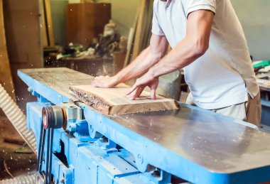 Bir adam, marangozluk atölyesindeki büyük bir endüstriyel ortaklığa tahta yerleştiriyor.