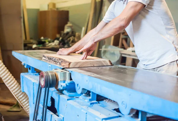 A man planes a board on a large industrial jointer in a carpentry workshop