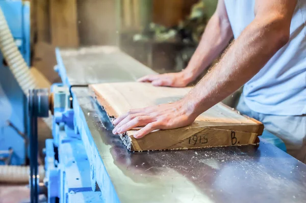 A man planes a board on a large industrial jointer in a carpentry workshop