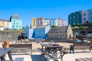 Tenby, Pembrokeshire, Güney Galler İngiltere - 2 Haziran 2025 St. Julian Kilisesi Tenby kumsalında renkli evler ve deniz kenarındaki bankların çerçevelediği