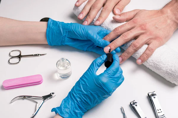 Men's manicure. Beautician in rubber gloves, apply a protective nail Polish.