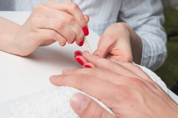Mannen manicure. de handen van de schoonheidsspecialiste behandeld cuticula van mannen handen met behulp van de oranje stokken — Stockfoto