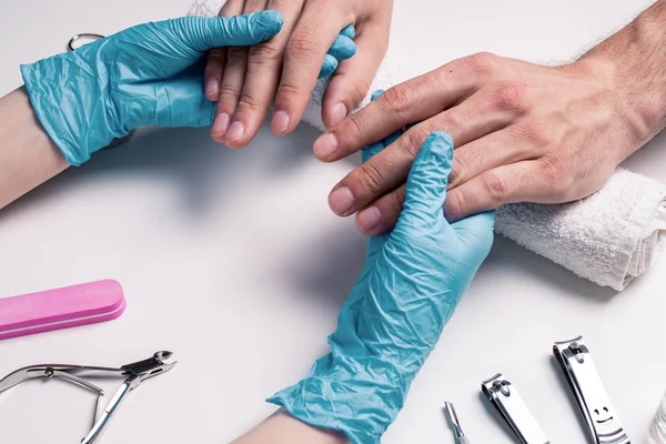 Mannen manicure. Schoonheidsspecialist in rubberen handschoenen onderzoekt de conditie van de nagels. — Stockfoto