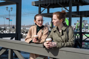 Tek kullanımlık bardak kahve ile sahildeki iki kadın konuşmak.