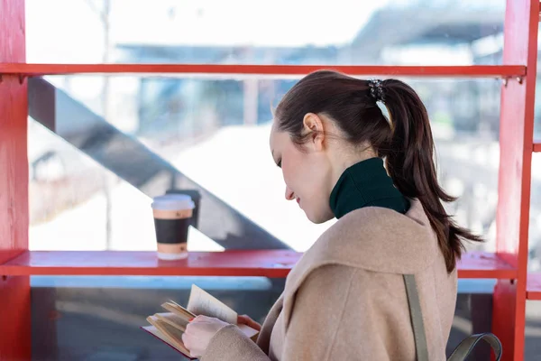 Молодая девушка, читающая книгу рядом с полками с кофе и книгами, социальная библиотека, место обмена книгами — стоковое фото