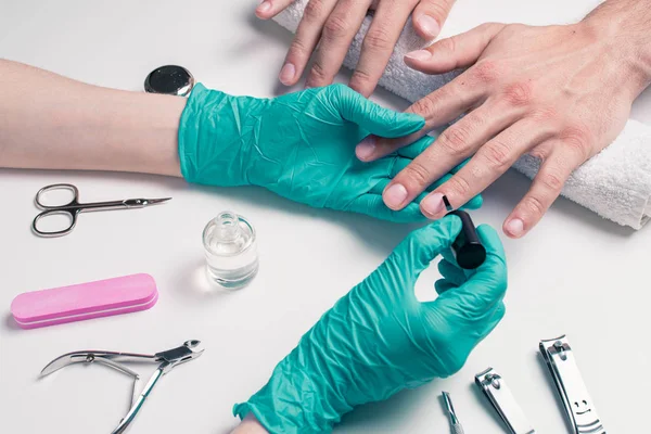 Mannen manicure. Schoonheidsspecialiste in rubberen handschoenen, toepassing een beschermende nagellak — Stockfoto