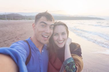 Neşeli selfie çift sahilde günbatımında gülümseyen
